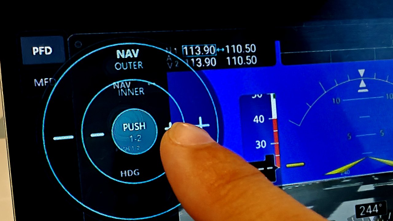 A finger turning the NAV knob on a G1000 panel shown on a touchscreen, with PanelSight's concentric rotation areas and their plus and minus buttons drawn around it